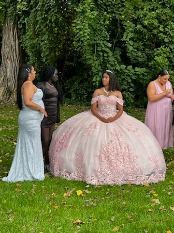 Quinceañera in pink floral ball gown with court in outdoor setting