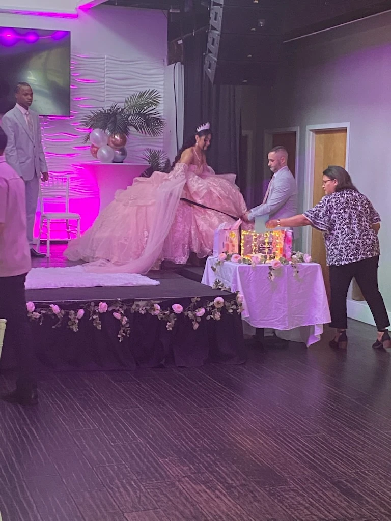 Quinceañera on stage in pink ball gown at reception