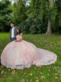 Quinceañera in pink ball gown with chambelan in park setting