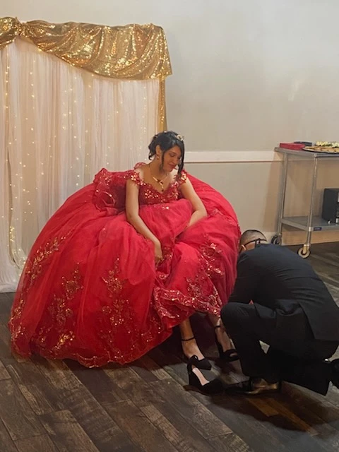 Quinceañera shoe ceremony in red ball gown with gold accents