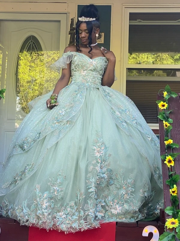 Quinceañera in sage green ball gown with floral embroidery on porch