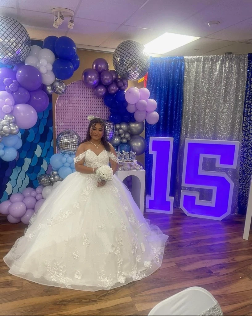 Quinceañera in white floral ball gown with purple and blue balloon decor